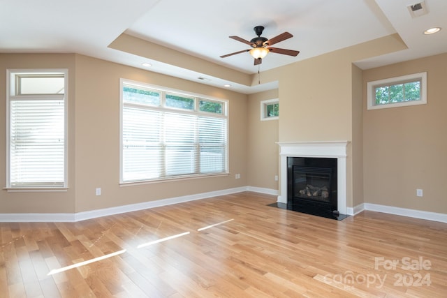 unfurnished living room featuring a raised ceiling, light hardwood / wood-style floors, and ceiling fan