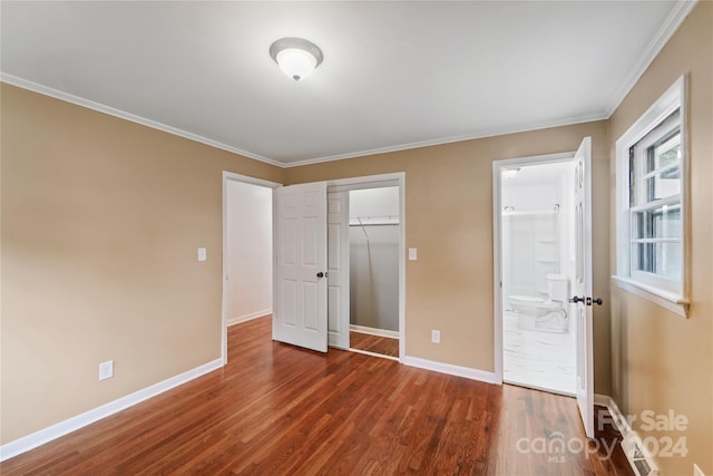 unfurnished bedroom with ensuite bath, a closet, crown molding, and dark wood-type flooring