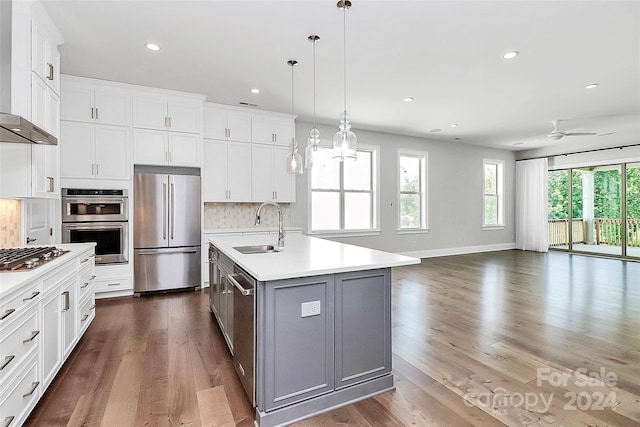 kitchen featuring sink, white cabinetry, hanging light fixtures, stainless steel appliances, and a center island with sink