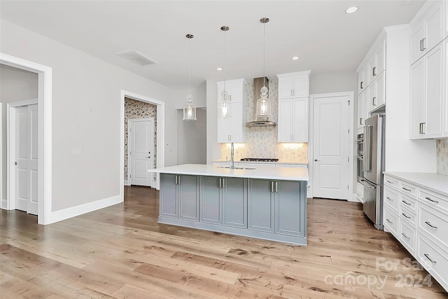 kitchen with white cabinets, a center island with sink, hanging light fixtures, and wall chimney range hood