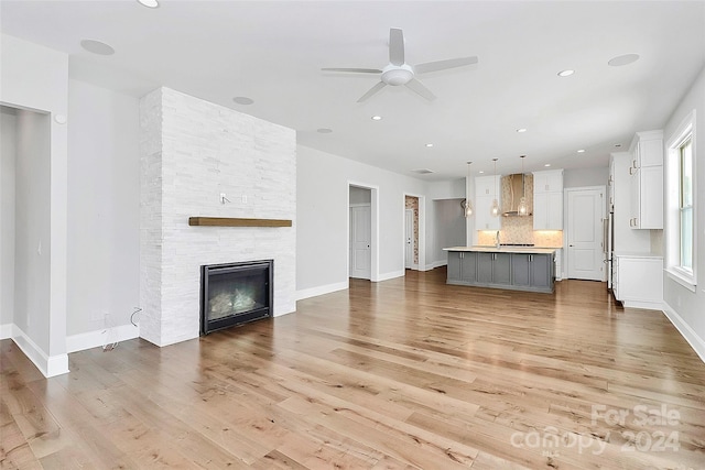 unfurnished living room with a stone fireplace, light hardwood / wood-style floors, and ceiling fan