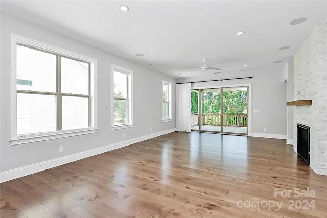 unfurnished living room featuring ceiling fan, hardwood / wood-style floors, and a stone fireplace