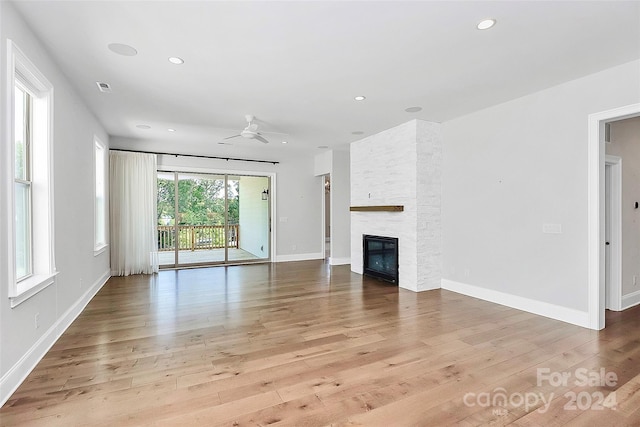 unfurnished living room with ceiling fan, a stone fireplace, and light wood-type flooring