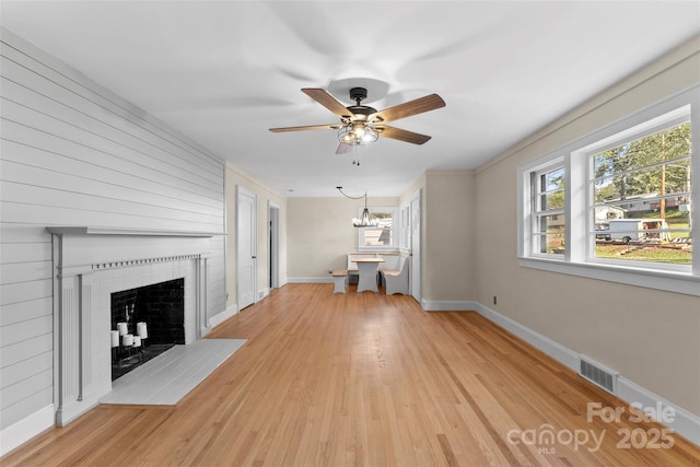 unfurnished living room featuring a fireplace, ceiling fan with notable chandelier, and light hardwood / wood-style flooring