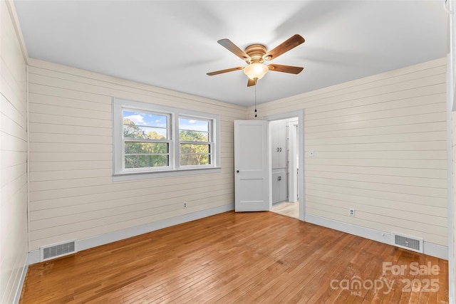 spare room with ceiling fan, light hardwood / wood-style floors, and wooden walls