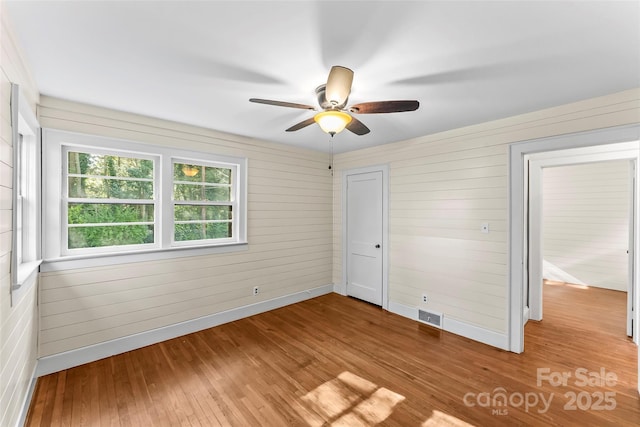 unfurnished bedroom with light hardwood / wood-style floors, ceiling fan, and wood walls