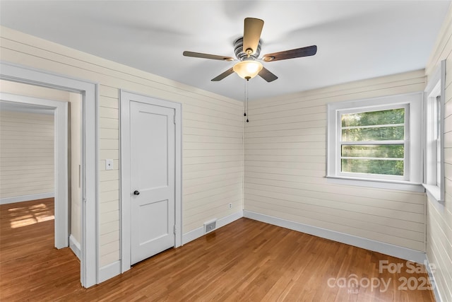 unfurnished bedroom featuring ceiling fan, wooden walls, and light hardwood / wood-style floors