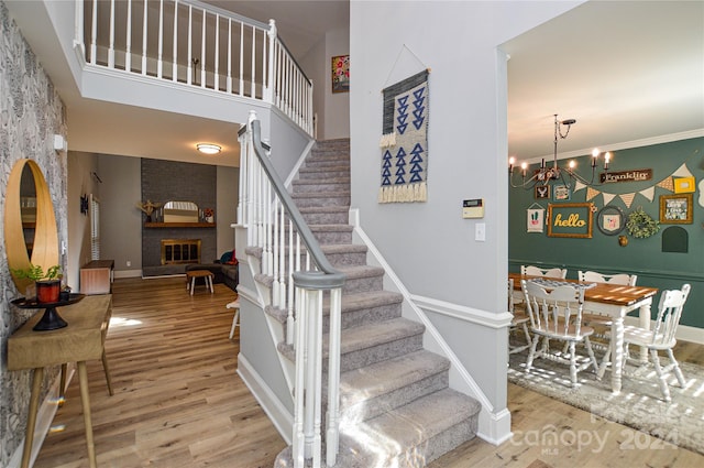 stairway featuring a high ceiling, an inviting chandelier, ornamental molding, a fireplace, and wood-type flooring