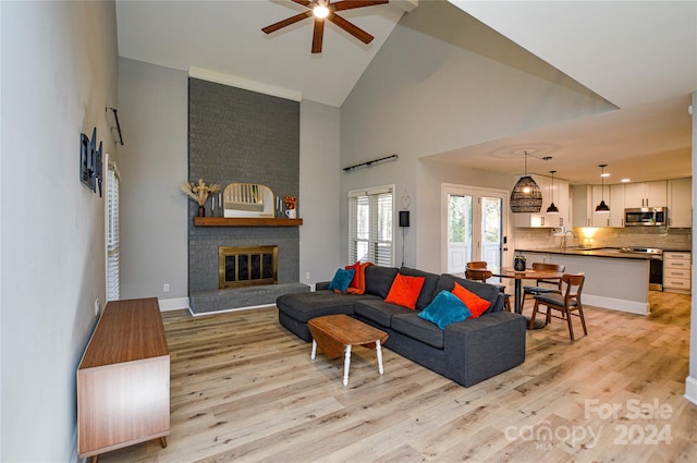 living room featuring a brick fireplace, ceiling fan, sink, high vaulted ceiling, and light hardwood / wood-style flooring