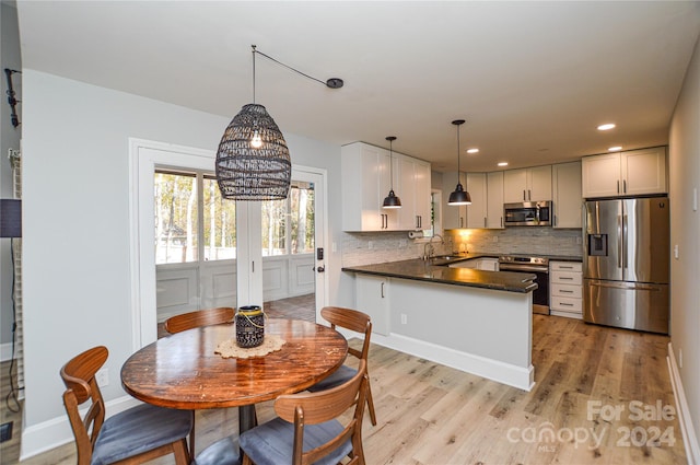 kitchen with pendant lighting, kitchen peninsula, light hardwood / wood-style floors, white cabinetry, and stainless steel appliances