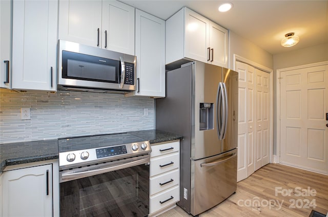 kitchen with dark stone countertops, white cabinetry, light hardwood / wood-style floors, and appliances with stainless steel finishes