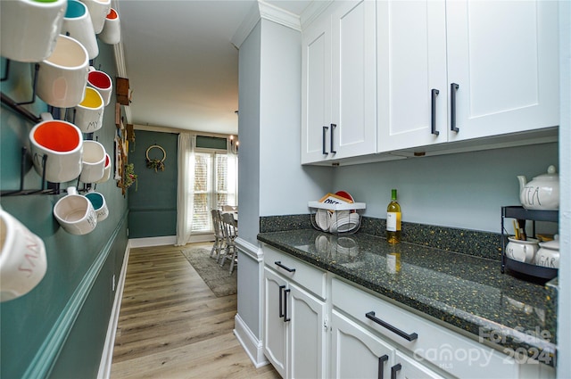 kitchen featuring white cabinets, light hardwood / wood-style floors, crown molding, and dark stone countertops