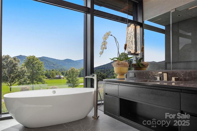 bathroom featuring vanity, a tub, floor to ceiling windows, and a mountain view