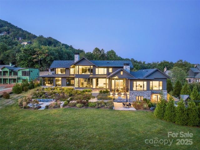 back house at dusk with a patio, a yard, and a mountain view