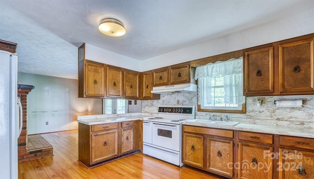 kitchen with a textured ceiling, light hardwood / wood-style flooring, kitchen peninsula, and white appliances