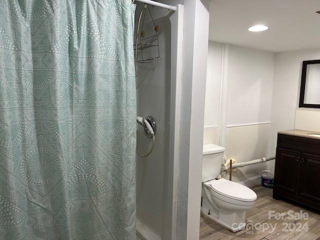 bathroom with wood-type flooring, curtained shower, vanity, and toilet