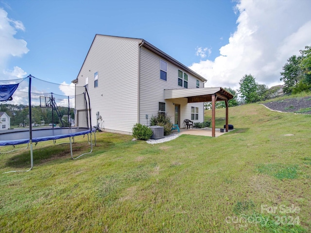 back of property with a trampoline, a yard, a patio area, and central AC