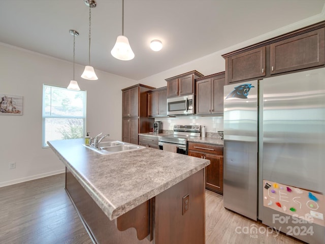 kitchen featuring appliances with stainless steel finishes, light hardwood / wood-style floors, an island with sink, decorative light fixtures, and sink