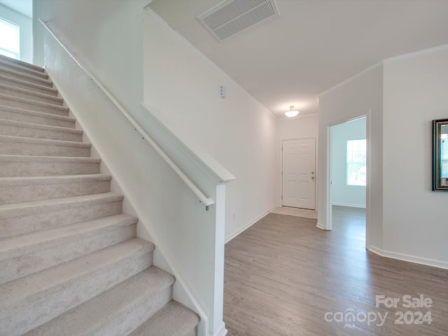 stairway with wood-type flooring and crown molding