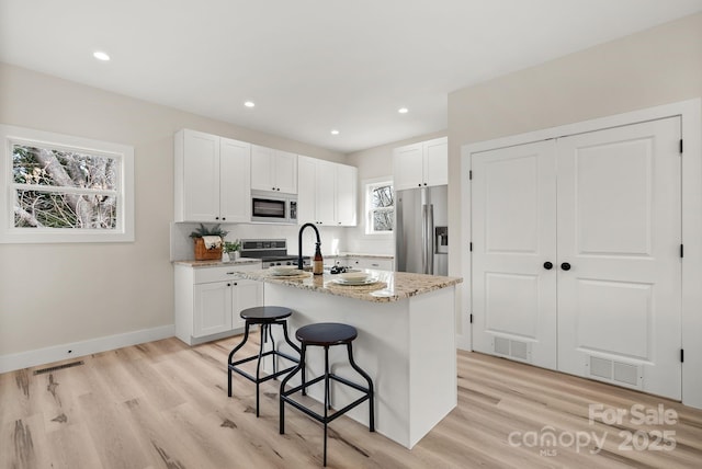 kitchen featuring light stone counters, appliances with stainless steel finishes, an island with sink, and white cabinetry