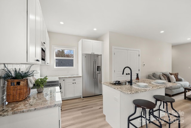 kitchen featuring appliances with stainless steel finishes, open floor plan, a kitchen island with sink, white cabinetry, and a sink