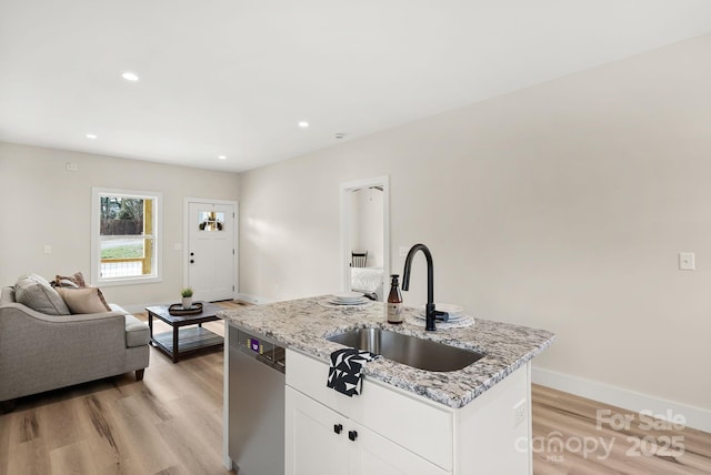 kitchen featuring a sink, white cabinets, open floor plan, stainless steel dishwasher, and an island with sink