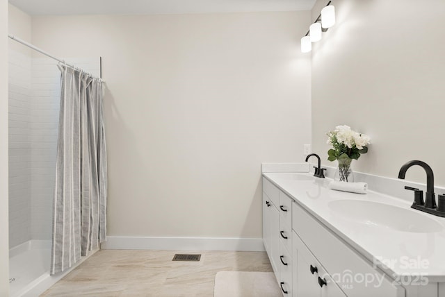 full bathroom featuring tiled shower, a sink, and double vanity