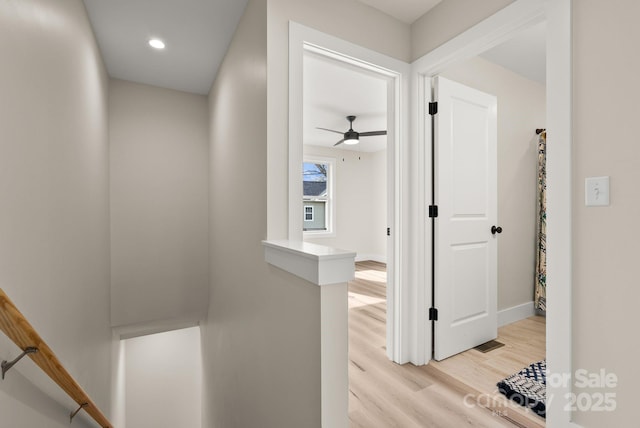 hall featuring light wood-type flooring, recessed lighting, baseboards, and an upstairs landing