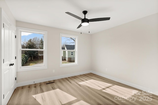 spare room featuring light wood finished floors, a ceiling fan, visible vents, and baseboards