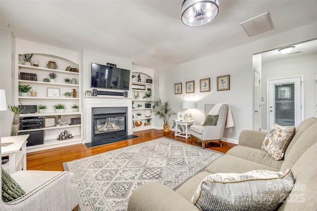 living area with a glass covered fireplace, visible vents, and wood finished floors