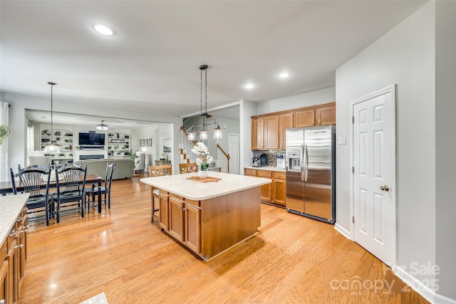 kitchen with light wood-type flooring, brown cabinets, hanging light fixtures, stainless steel refrigerator with ice dispenser, and open floor plan