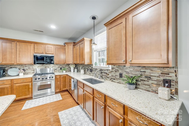 kitchen featuring a sink, visible vents, appliances with stainless steel finishes, light wood finished floors, and decorative light fixtures