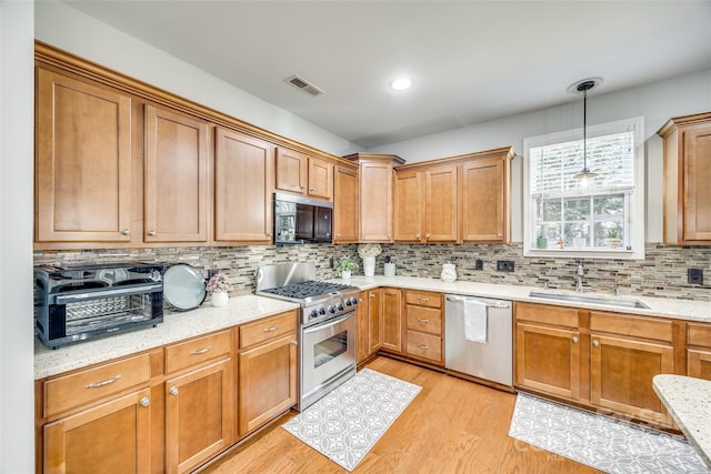 kitchen featuring stainless steel appliances, tasteful backsplash, visible vents, light wood-style floors, and a sink