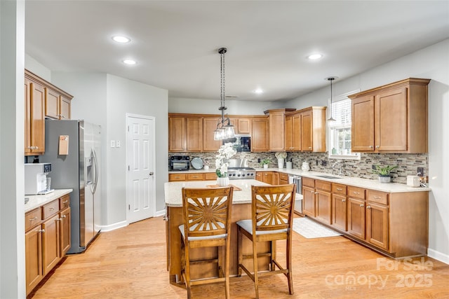 kitchen featuring brown cabinets, decorative light fixtures, backsplash, light wood-style floors, and stainless steel fridge