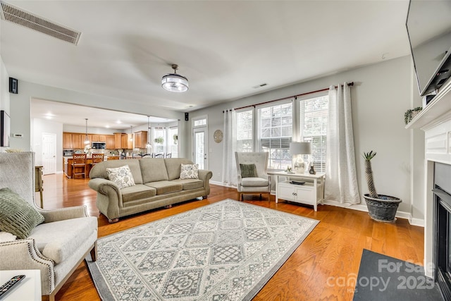 living room featuring light wood-type flooring, a fireplace with flush hearth, visible vents, and baseboards