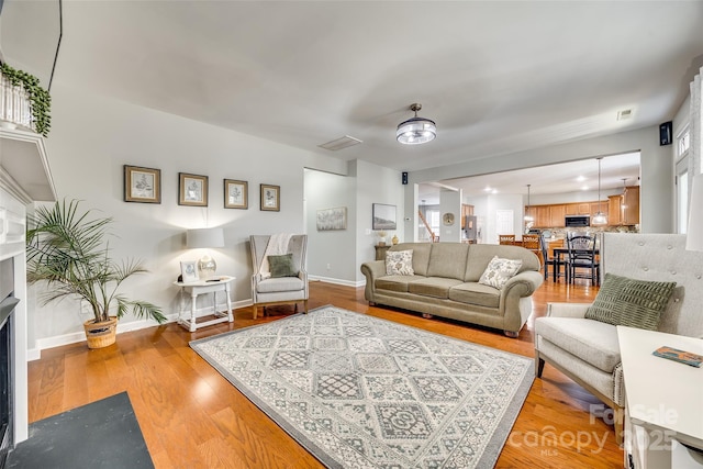 living area featuring light wood finished floors, stairway, visible vents, and baseboards