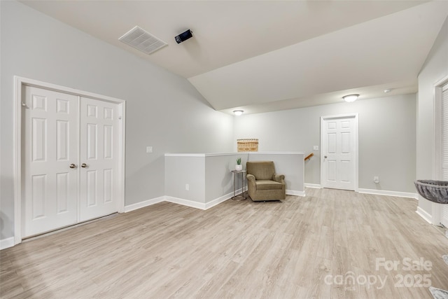 unfurnished room featuring wood finished floors, visible vents, baseboards, vaulted ceiling, and an upstairs landing