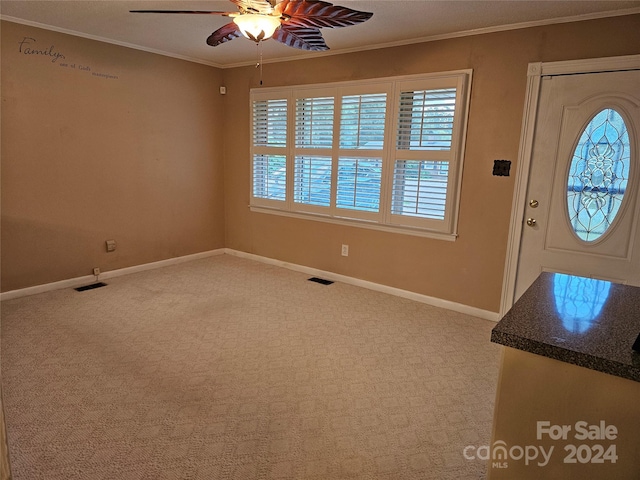 entrance foyer with carpet flooring, ornamental molding, and ceiling fan