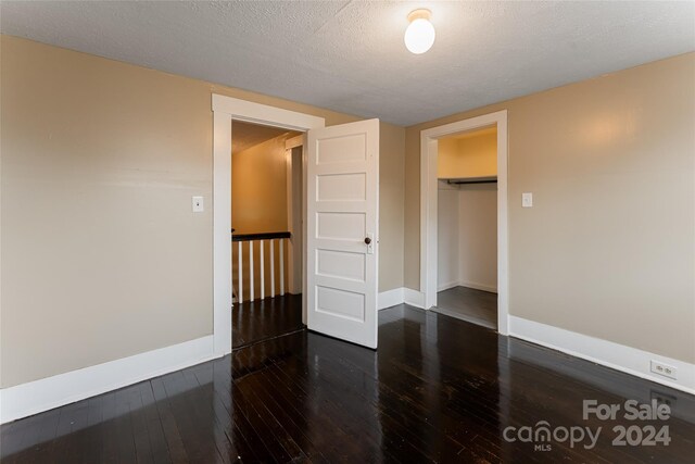 unfurnished bedroom featuring a textured ceiling, a closet, and dark hardwood / wood-style flooring