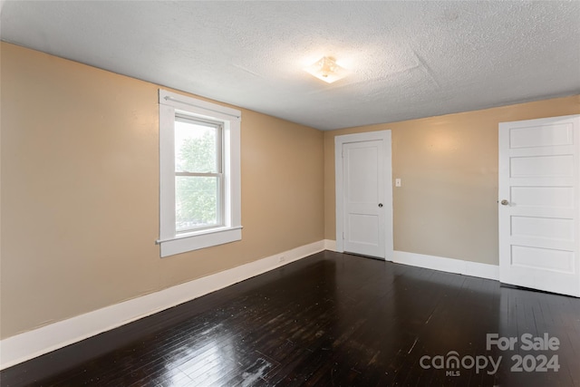 empty room with a textured ceiling and dark hardwood / wood-style flooring