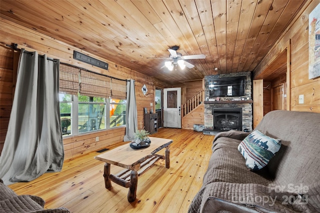 living room with ceiling fan, wooden ceiling, a stone fireplace, wood walls, and hardwood / wood-style flooring