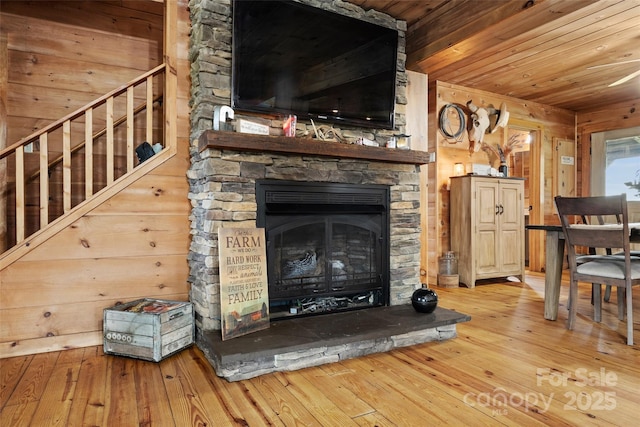 unfurnished living room with light wood-type flooring, a stone fireplace, wooden walls, and wood ceiling