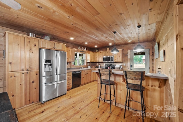 kitchen with black appliances, light brown cabinetry, decorative light fixtures, light hardwood / wood-style floors, and a kitchen bar