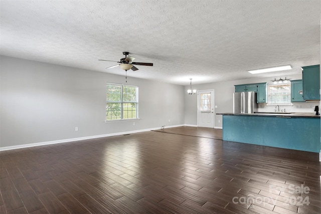 unfurnished living room with a textured ceiling, ceiling fan with notable chandelier, sink, and dark wood-type flooring