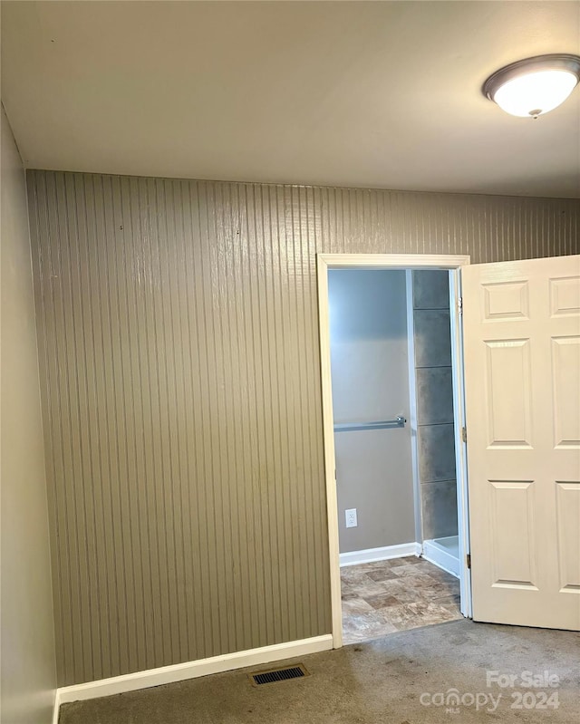 carpeted empty room featuring wood walls