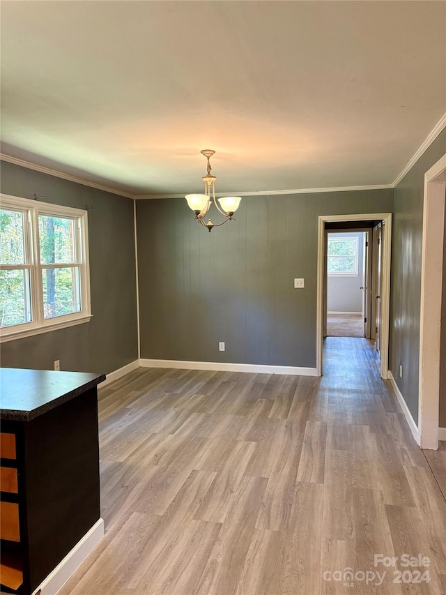 unfurnished dining area with crown molding, a healthy amount of sunlight, an inviting chandelier, and light wood-type flooring