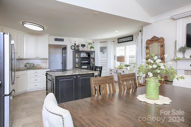 kitchen with white cabinetry, a center island, light stone counters, and stainless steel refrigerator