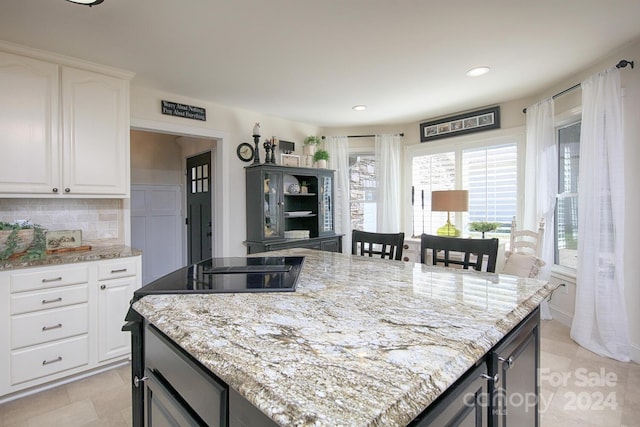 kitchen featuring light stone countertops, white cabinetry, a kitchen island, and tasteful backsplash