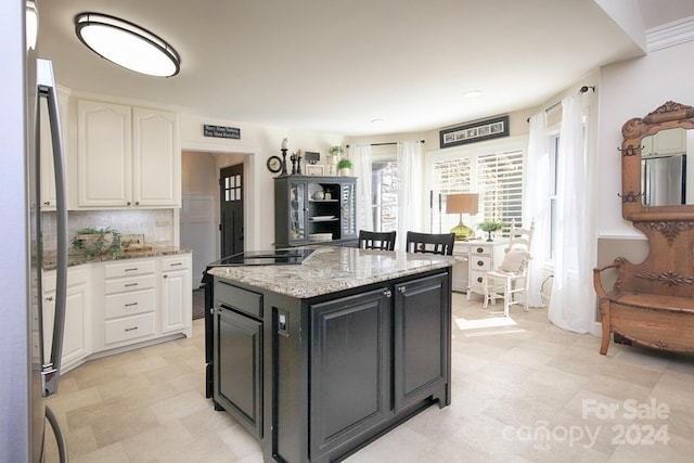 kitchen featuring a kitchen island, stainless steel fridge, white cabinetry, and light stone counters