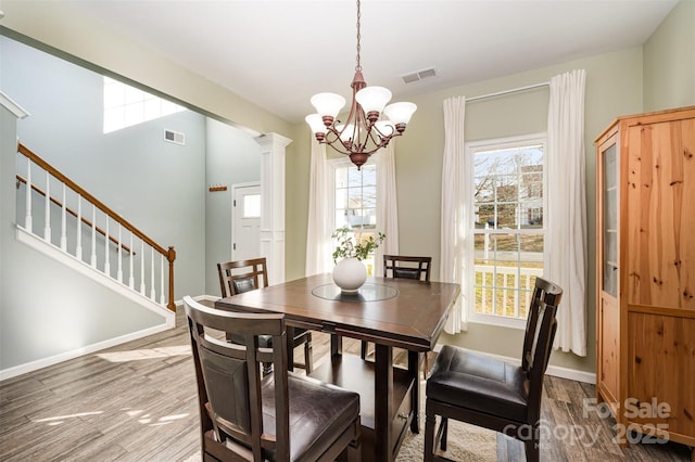 dining area with a healthy amount of sunlight, a chandelier, wood-type flooring, and decorative columns